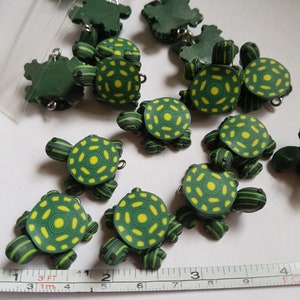 Puede incluir: Una colección de 10 dijes de tortuga verde y amarilla con rayas negras. Las tortugas tienen un patrón de caparazón detallado y están hechas de arcilla polimérica. Los dijes miden aproximadamente 2,5 cm.