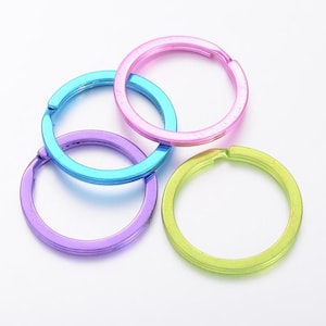 Può includere: Quattro portachiavi colorati nei toni del blu, viola, rosa e verde. Gli anelli sono realizzati in un materiale metallico lucido e sono disposti in modo leggermente sovrapposto su sfondo bianco.