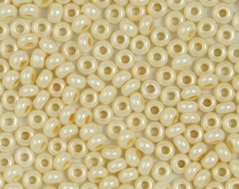 May include: A close-up image of a large quantity of small, round, cream-colored beads. The beads have a hole in the center and a slightly iridescent finish.