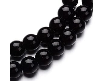 Puede incluir: Primer plano de un collar de cuentas negras brillantes. Las cuentas son perfectamente redondas y reflejan la luz, creando una apariencia brillante. Las cuentas están ensartadas, lo que sugiere que son parte de un collar o pulsera.