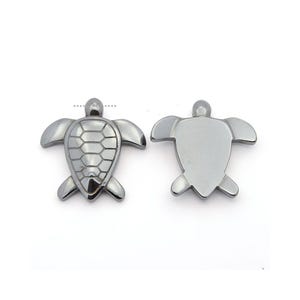 May include: Two silver-toned turtle charms, one with a detailed shell design and the other with a smooth surface.