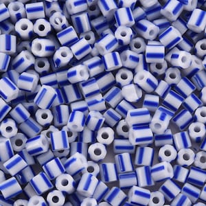 May include: A close-up of a collection of white and blue striped beads. The beads are cylindrical with a hole through the middle. Each bead has blue stripes evenly spaced around its circumference. These beads are ideal for jewellery making and crafts.