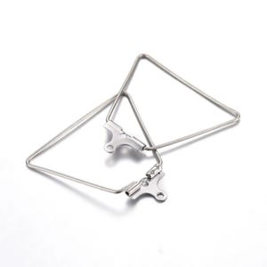 May include: Two silver-colored, triangular earring findings. Each finding has a geometric shape with a hinged clasp. The earrings are displayed on a white background.