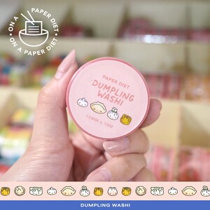 May include: A pink washi tape roll with the text "Paper Diet Dumpling Washi" and dumpling illustrations. The tape is 15mm x 10m. The image also includes the text "On a Paper Diet" in a circular logo.