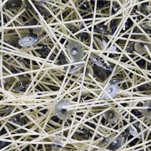 May include: Close-up of a pile of candle wicks and wick holders. The wicks are a light beige color, and the metal holders are silver. The wicks are intertwined, creating a dense, textured pattern. The image suggests materials for candle making.