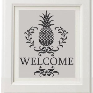 May include: A framed wall art piece featuring a black pineapple design with the word "WELCOME" in a decorative font. The pineapple is surrounded by floral elements. The frame is white.