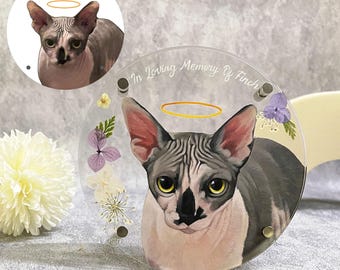 Op de afbeelding: Een heldere, ronde gedenkplaat met een portret van een Sphynx-kat en een halo. De plaat bevat de tekst "In Loving Memory Of Finch" en is versierd met gedroogde bloemen. De kat heeft grijs en wit haar.