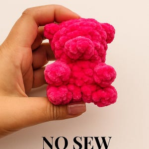 Könnte beinhalten: Ein hellrosa, nahtloser, gehäkelter Teddybär. Das Plüschtier wird in einer Hand vor einem hellen Hintergrund gehalten. Der Text "PDF PATTERN" und "NO SEW" ist in Schwarz gedruckt.
