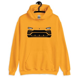 Könnte beinhalten: Senfgelber Kapuzenpullover mit schwarzer Grafik eines Fahrzeugfrontendesigns. Das Design umfasst Scheinwerfer, einen Kühlergrill und eine Stoßstange. Der Hoodie hat eine Kapuze mit Kordelzug und eine Vordertasche.