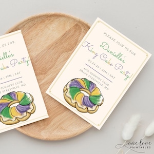 May include: Two cream-colored invitations with gold borders and a watercolor illustration of a King Cake. The text reads "Please join us for Danielle's King Cake Party!" with date, time, and location details. The invitations are on a wooden tray.