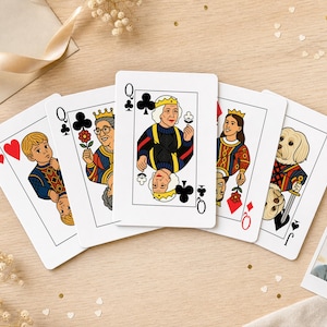 May include: A set of five custom playing cards featuring illustrated characters including a young person, a person with glasses, a person with a crown, a person with long hair, and a dog, alongside a small square photograph of a person.