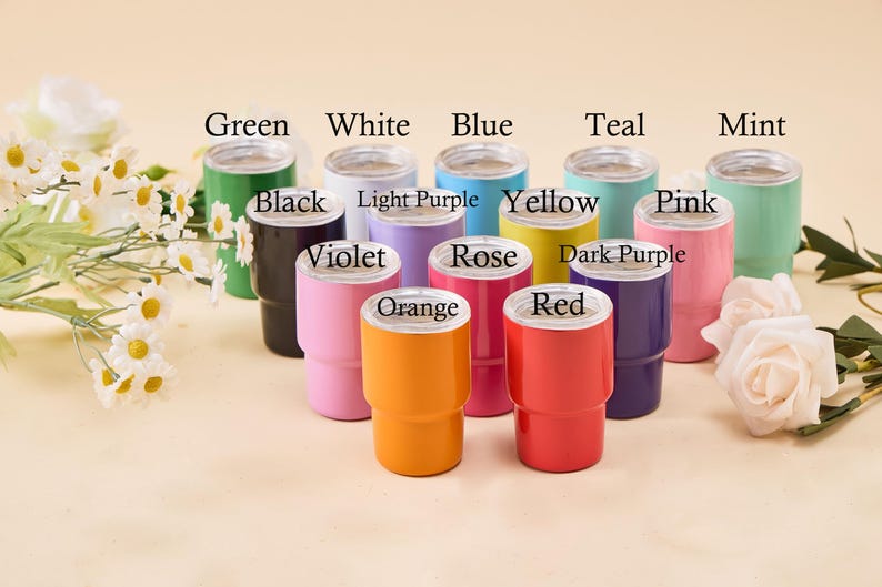 May include: A collection of insulated tumblers in various colors, including green, white, blue, teal, and mint. Each tumbler has a silver rim and is labeled with its color name. The tumblers are arranged with floral accents.