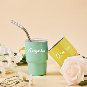 May include: Two personalized tumblers, one mint green and one yellow, with white text. The mint green tumbler has a silver straw. The text on the mint green tumbler says "Angela", and the yellow tumbler says "Armica".