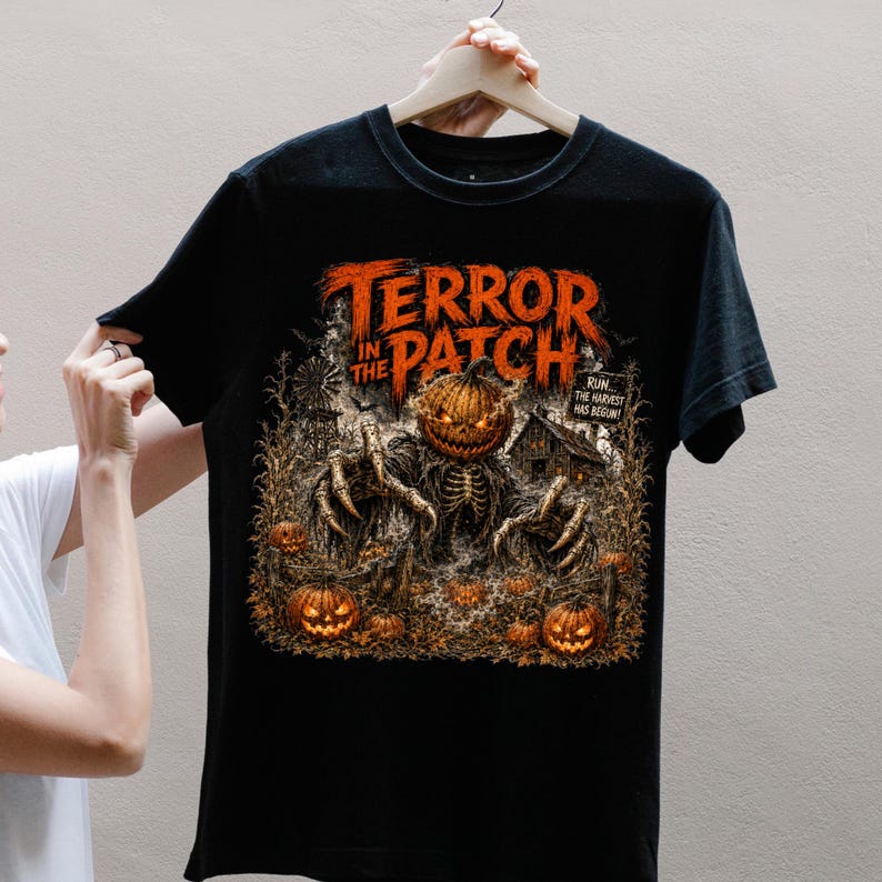 May include: A black short-sleeve t-shirt featuring a graphic print of a skeletal creature with a pumpkin head in a field. The text reads TERROR IN THE PATCH and RUN... THE HARVEST HAS BEGUN! The design includes orange pumpkins and a dark barn.