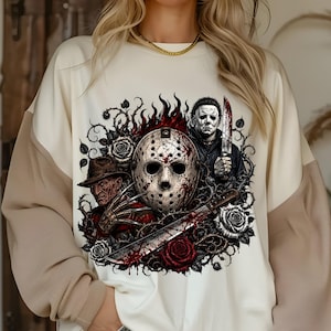 May include: A cream-colored sweatshirt featuring a graphic print of three horror movie characters: a hockey mask, a man in a fedora with clawed gloves, and a man holding a knife. The design includes red roses, thorny vines, and flames.