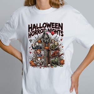 May include: A white t-shirt featuring a graphic print with the text "HALLOWEEN HORROR NIGHTS" above a stack of vintage televisions. Each screen displays a different horror character, surrounded by pumpkins, skulls, and a red balloon.