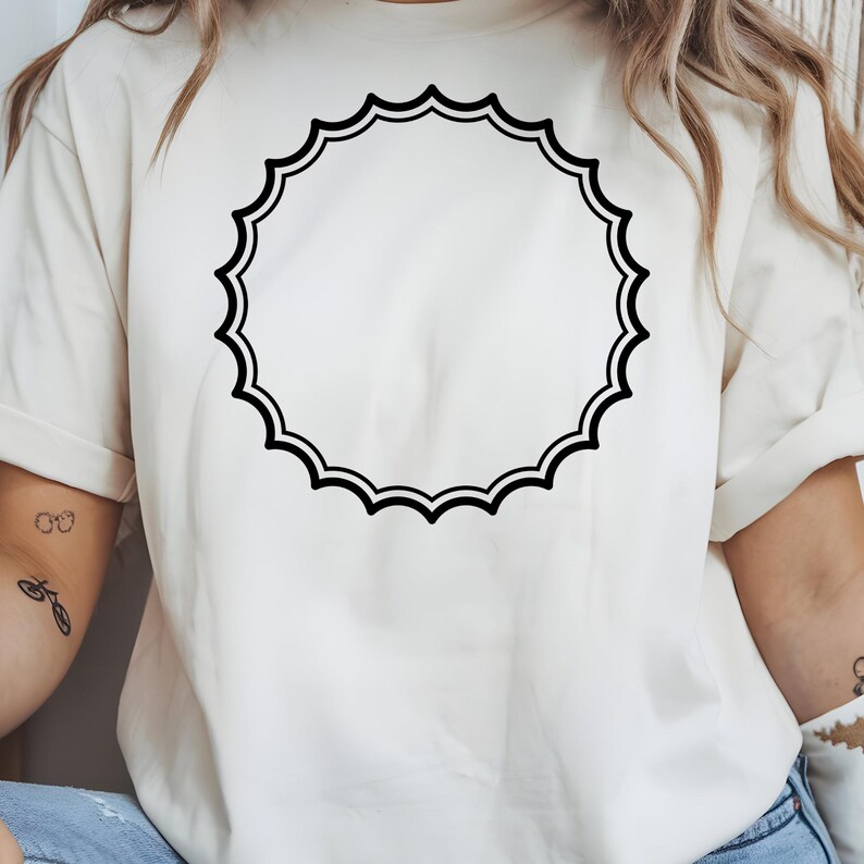 May include: Cream-colored t-shirt featuring a large, black, scalloped circle design. The design is centered on the shirt, creating a simple yet eye-catching graphic. The shirt has short sleeves and a relaxed fit, suitable for casual wear.