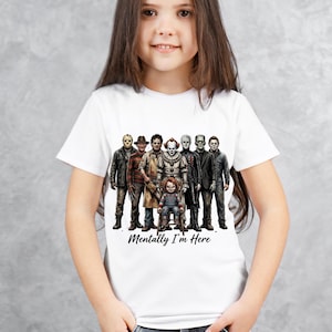 May include: A white short-sleeved t-shirt featuring a graphic print of various horror movie characters standing together, with a small doll figure sitting in front. The text "Mentally I'm Here" is printed in a black script font below the characters.