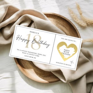 May include: A white birthday scratch card with gold details, featuring the text "Happy Birthday" and "18". The card includes a gold heart with "Paris with Friends" and a scratch area. The card is on a wooden plate.