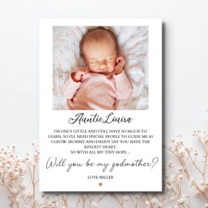 Op de afbeelding: Een rechthoekige kaart met een foto van een slapende baby in een roze outfit. De tekst luidt: Auntie Louisa, I'm only little and still have so much to learn, so I'll need special people to guide me as I grow. Mummy and daddy say you have the kindest heart. So with all my tiny hope... Will you be my godmother? Love Miller.