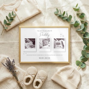 May include: A framed print with three monochrome baby photos, the text "THE DAY YOU BECAME MY Daddy", and the name "NOAH JACOB". The frame is surrounded by baby clothes, a hat, shoes, and eucalyptus.