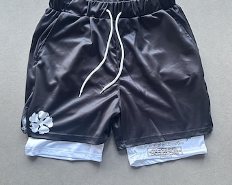 Zwei-in-Eins-Shorts für Herren mit einem schwarzen Totenkopf mit Hörnern und einem vierblättrigen Kleeblatt als Aufdruck auf der Innenseite, voller lustiger Anime-Magie-Stil.