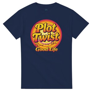 Könnte beinhalten: Marineblaues T-Shirt mit einem kreisförmigen Grafikdesign. Die Grafik zeigt die Worte "Plot Twist" in Gelb und Orange, darunter "This is the Good Life". Das T-Shirt hat einen Rundhalsausschnitt und kurze Ärmel.