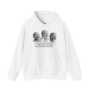 May include: White hooded sweatshirt with a front pocket and drawstring. The front features a graphic of three smiling babies and the text "NICHE BABY" in a rectangular box. The sweatshirt is a casual style.