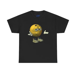 May include: Black t-shirt featuring a yellow emoji character with a skeptical expression, arms outstretched, and wearing sneakers. The emoji has a 3D design. The shirt has a small logo on the upper back.