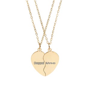 May include: Two gold-colored necklaces with heart-shaped pendants. Each pendant is engraved with the words "Chopped" and "Une" on each half of the heart. The necklaces have delicate chain links.