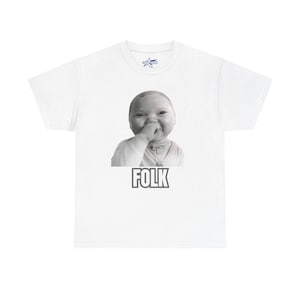 May include: White t-shirt featuring a black and white image of a baby with their hand near their mouth. The word "FOLK" is printed in a bold, black font below the image. A small logo is visible on the upper chest.