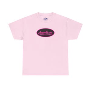 May include: A light pink t-shirt with a black oval design in the center. The oval has a pink border and the words "chopped & unc" in pink script. A small star graphic is above the oval.
