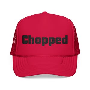 May include: A red trucker hat with a mesh back and a curved brim. The word "chopped" is printed in black, block letters across the front of the hat. The hat is a vibrant shade of red.