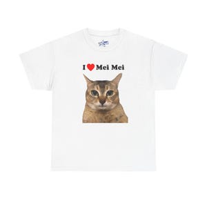 Könnte beinhalten: Weißes T-Shirt mit einem Katzenkopf und dem Text "I ❤️ Mei Mei" in Schwarz und Rot. Die Katze hat braunes und beiges Fell und grüne Augen. Das Shirt hat einen Rundhalsausschnitt und kurze Ärmel.
