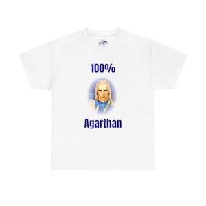 May include: White t-shirt with the text "100% Agarthan" in blue. The shirt features a graphic of a person with long blonde hair and a blue and gold outfit. The shirt has a crew neck and short sleeves.
