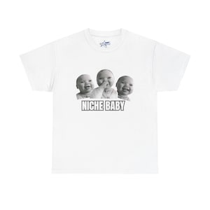 May include: White t-shirt featuring a graphic of three babies with the text "NICHE BABY" in a bold, sans-serif font. The babies are in black and white, with one baby touching their face. The shirt is a classic crew neck.