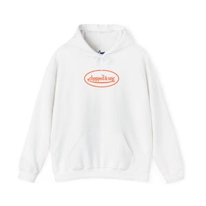 May include: A white hoodie with a front pocket and a drawstring hood. The sweatshirt has an orange oval logo with the words "chopped & unc" in a stylized font.