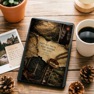May include: A rectangular e-reader device displaying a fantasy-themed graphic featuring a gold ring on a chain, a map, and the text "NOT ALL THOSE WHO WANDER ARE LOST. - J.R.R. TOLKIEN" layered over images of a mountain landscape and a dark tower.