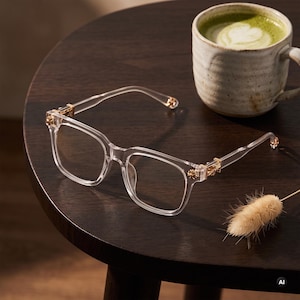 May include: Clear transparent eyeglasses with a square frame shape. The temples feature metallic gold-toned cross-shaped decorative accents at the hinges. The glasses have clear lenses and are constructed from a smooth, translucent material.