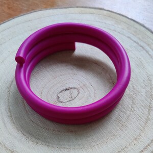May include: A bright pink rubber bracelet, coiled into a circle, on a wooden surface.