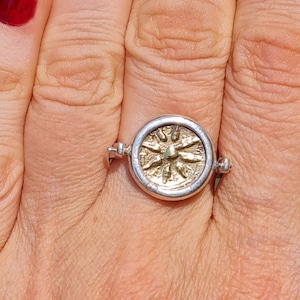 Può includere: Un anello d'argento con una moneta d'oro rotante che presenta un design solare stilizzato.