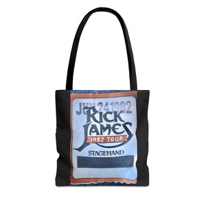May include: Black tote bag featuring a vintage concert ticket design. The ticket reads "JUN 24 1982" and "Rick James 1982 Tour Stagehand". The bag has black handles and a black body.