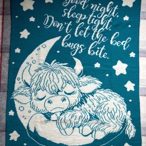 Puede incluir: Manta de punto color turquesa con una vaca de las Tierras Altas durmiendo sobre una luna creciente, rodeada de estrellas blancas. El texto "Good night, sleep tight, Don't let the bed bugs bite" está escrito en blanco. Un artículo decorativo y acogedor.