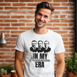Könnte beinhalten: Weißes T-Shirt mit einer Schwarz-Weiß-Grafik von drei Männern und dem Text "IN MY Progressive ERA". Das Shirt besteht aus einem weichen Material und eignet sich für Freizeitkleidung.