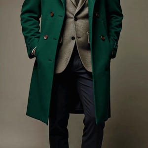 Op de afbeelding: Een dubbelbrede, smaragdgroene overjas met bruine knopen. De jas wordt gedragen over een grijs colbert, een wit overhemd en een zwarte stropdas. De outfit wordt gecompleteerd met een marineblauwe broek.