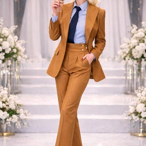May include: A tailored, tan-colored suit with a matching blazer and high-waisted pants. The suit is paired with a light blue button-down shirt and a patterned tie. The outfit is completed with tan heels.