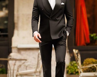 Puede incluir: Un traje negro de doble botonadura con camisa blanca, pajarita negra y zapatos de cuero negro. El traje tiene solapa de satén y se lleva con un pañuelo blanco. El hombre lleva gafas de sol y un reloj de pulsera.