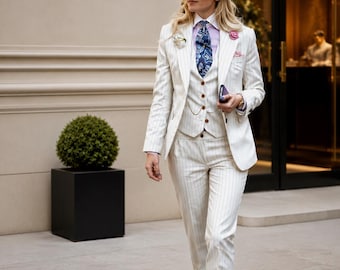 May include: A cream-colored pinstripe suit with a matching vest and pants. The outfit includes a white hat with a black band, a patterned tie, and a pink pocket square. The suit is worn with white shoes. The storefront behind the person says "MARICLOTHIG".