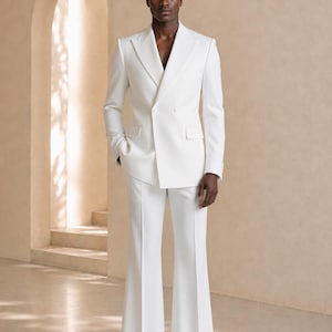 Può includere: Un completo bianco doppiopetto composto da una giacca sartoriale con ampi revers a lancia e due tasche con patta, abbinato a pantaloni svasati coordinati caratterizzati da una piega stirata lungo il centro di ogni gamba.