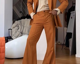 May include: A burnt orange suit with a matching blazer and flared pants. The suit is paired with a cream-colored button-up shirt and a gold necklace. The outfit is a stylish ensemble.